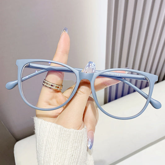 Black full-frame round anti-blue light glasses held by a hand with a gold ring and light blue gradient nails.