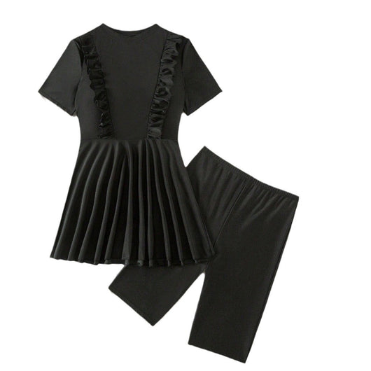 Woman in a black short-sleeve swim dress with ruffled details and matching swim shorts on a sandy beach. - Image 6