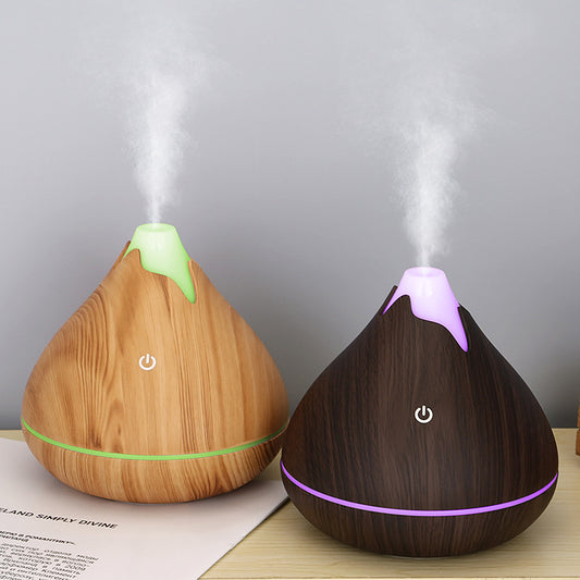 Teardrop-shaped aromatherapy humidifier with light wood grain finish, emitting mist and glowing with purple LED light.