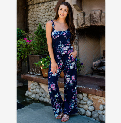 Woman wearing a navy blue floral wide-leg jumpsuit with pink and white flowers, tie-shoulder straps, and a drawstring waist. - Image 9