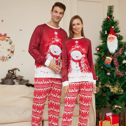 Family of four wearing matching red Christmas pajamas with snowman tops and reindeer fair isle pants, sitting by a Christmas tree.