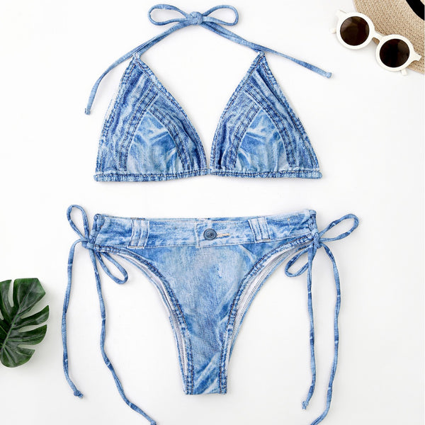 Women's light blue denim print two-piece bikini swimsuit with a halter neck top and tie-side bottoms, styled with a straw hat and sunglasses.