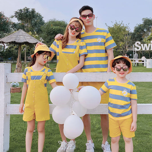 Family of four wearing matching yellow and blue striped t-shirts with daisy appliques. Mother and daughter wear yellow short overalls, father and son wear yello - Image 3