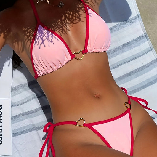 Pink and red halter-style triangle bikini with heart-shaped hardware and tie-up thong bottom, worn on a beach.