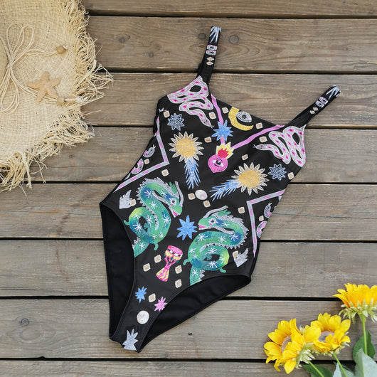 Black one-piece swimsuit for women featuring a vibrant multi-color print with dragons, suns, moons, and stars. - Image 2