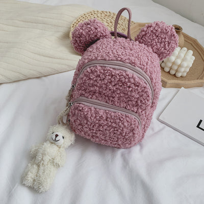 Pink fuzzy mini backpack with bear ears and a small white teddy bear keychain on a white bed. - Image 8