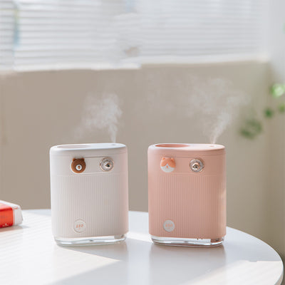 White cylindrical humidifier with ribbed texture, clear base, brown bear button, and silver dial, emitting mist on a white table.