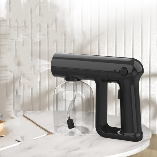 Black wireless alcohol blue light disinfection spray gun with clear reservoir, actively misting, on a marble surface. - Image 4