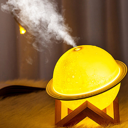 Yellow planet-shaped humidifier with a wooden stand emitting mist, next to a dark blue celestial gift bag. - Image 6