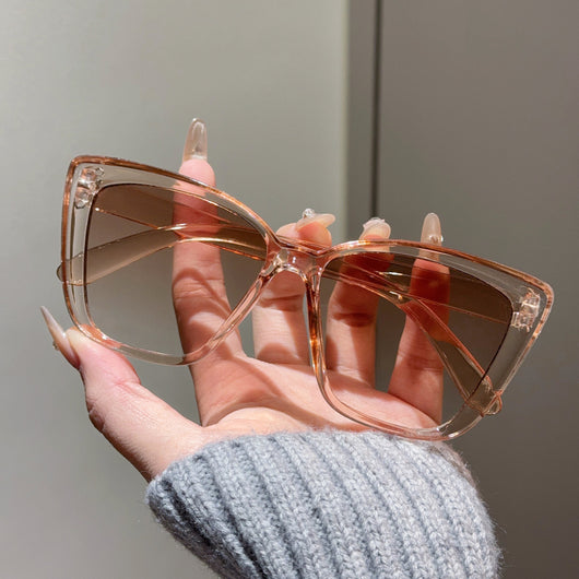 Clear large-frame square glasses held by a hand in a grey knitted sweater, showcasing the transparent plastic frame. - Image 10