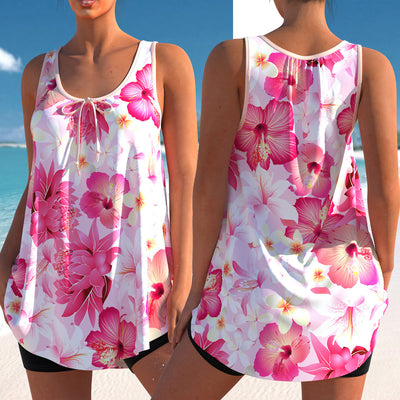 Woman wearing a pink and white floral print tankini top with black swim shorts on a sunny beach.