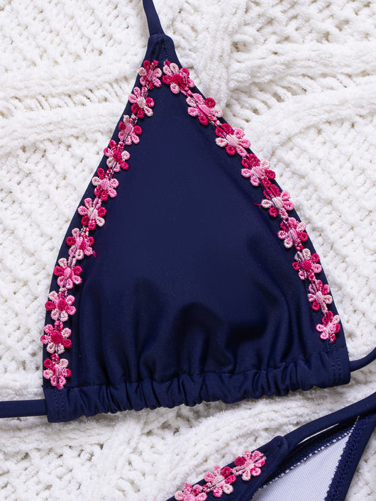 Navy blue bikini swimsuit set with pink floral lace trim on triangle top and tie-side bottoms, on a white knit blanket. - Image 14