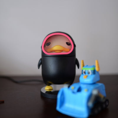 Black diving duck spray humidifier with red goggles and yellow feet, standing on a dark base on a table. - Image 3