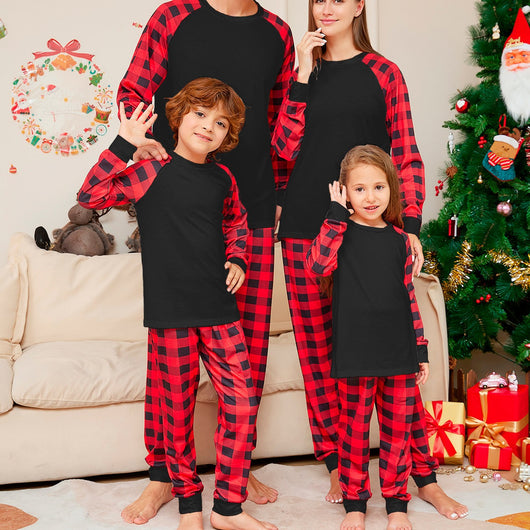 Family of four wearing matching black and red buffalo plaid pajamas in a festive Christmas living room.