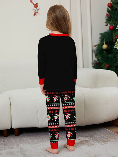 Man wearing black Christmas pajamas with a cartoon dinosaur, Santa Claus, and "Merry Christmas" text, standing by a decorated tree. - Image 26