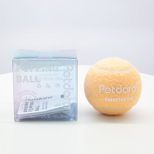 Peach yellow Petdora high elastic tennis ball dog toy next to its clear iridescent 'Popping Ball' packaging. - Image 4