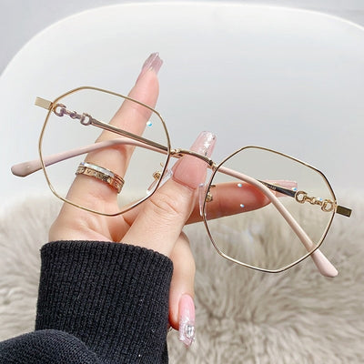 Rose gold frameless polygon anti-blue light glasses with clear lenses, held by a hand with pink nails.