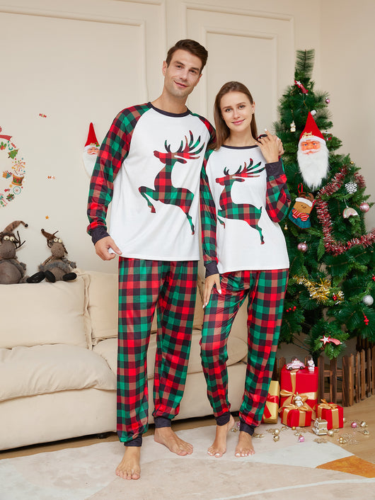 Two children in matching red and green plaid Christmas pajamas with a reindeer graphic, standing by a Christmas tree. - Image 3