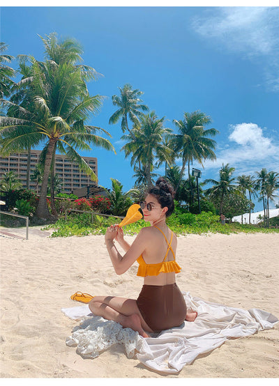 Woman in a yellow ruffled bikini top and dark brown high-waisted bottoms sitting on a beach. - Image 10