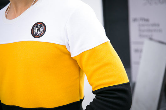 Men's white and yellow color block long-sleeve top with a crew neck and circular embroidered patch on the chest. - Image 10