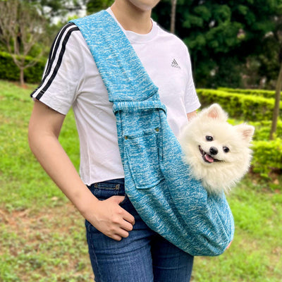 Person in white hoodie carrying a happy white dog in a navy blue pet sling bag outdoors. - Image 16