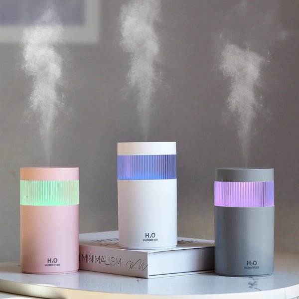 Light pink mini desktop USB humidifier with a blue LED light band and "H₂O HUMIDIFIER" text on the front.