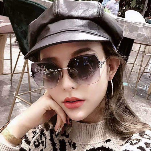 Woman wearing oversized hexagonal rimless sunglasses with gradient lenses and a black leather newsboy cap.