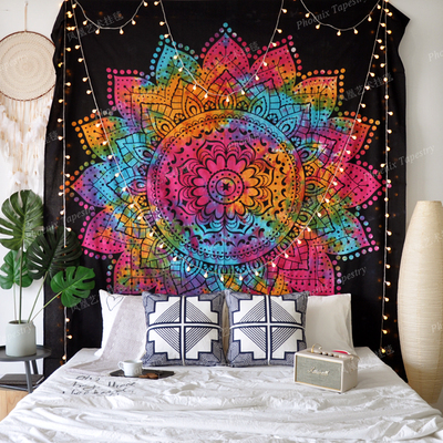 Vibrant mandala tapestry with a rainbow of colors on a black background, adorned with string lights, hanging above a bed.