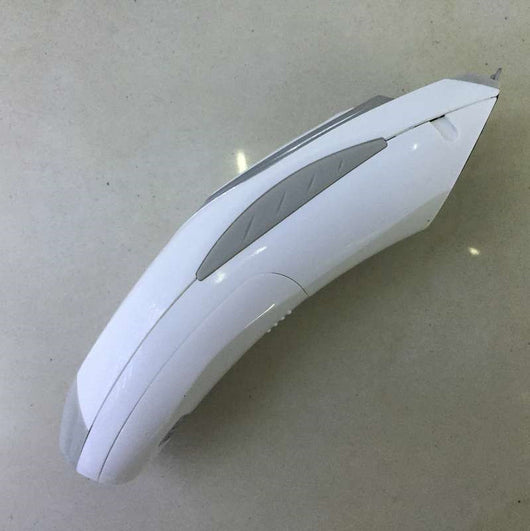 White and silver electric hair clipper held in hand, with a grey guide comb and blue packaging on a woven surface.