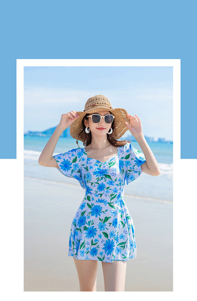 Woman in a light blue floral dress-style swimsuit with short sleeves and a sweetheart neckline on a beach. - Image 14
