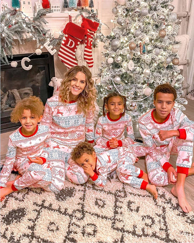 Family of four wearing matching green Christmas pajamas with white snowflakes and trees, red trim, sitting on a bed. - Image 7