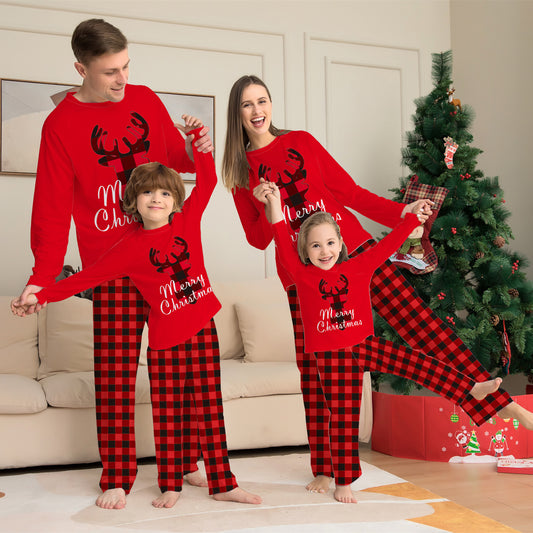 Family of four wearing matching red and black buffalo plaid Christmas pajamas with reindeer and "Merry Christmas" text.