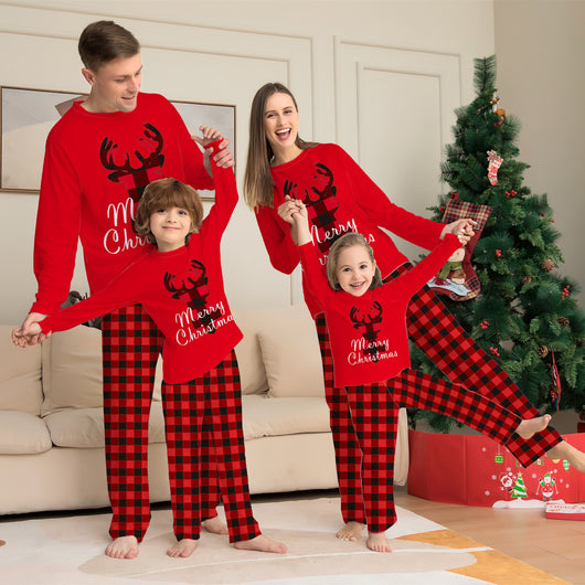Family of four wearing matching red and black buffalo plaid Christmas pajamas with reindeer and "Merry Christmas" text.