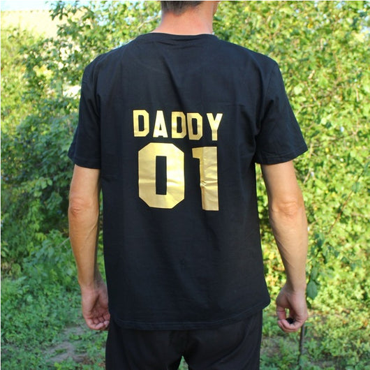 Child's black short-sleeved t-shirt with 'BABY 04' in gold print on the back, worn by a toddler in grass. - Image 9