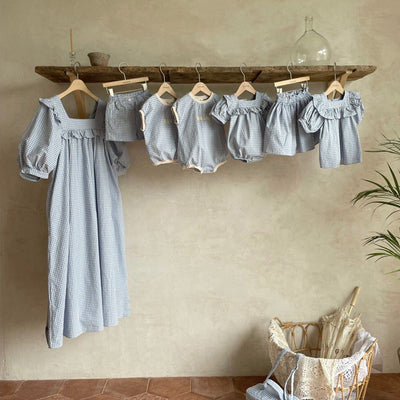 Light blue and white gingham baby romper with puff sleeves and ruffled square neckline, hanging on a wooden chair.