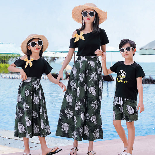 Family of four in matching black and green tropical print outfits on a beach, featuring t-shirts, shorts, skirt, and wide-leg pants. - Image 18