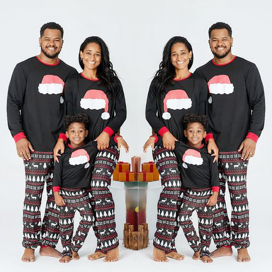 Family of three wearing matching black Christmas pajamas with Santa hat tops and reindeer fair isle pants.