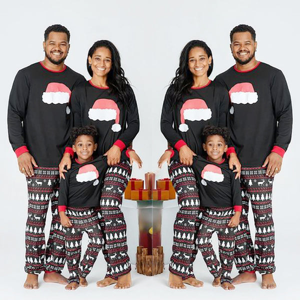Family of three wearing matching black Christmas pajamas with Santa hat tops and reindeer fair isle pants.