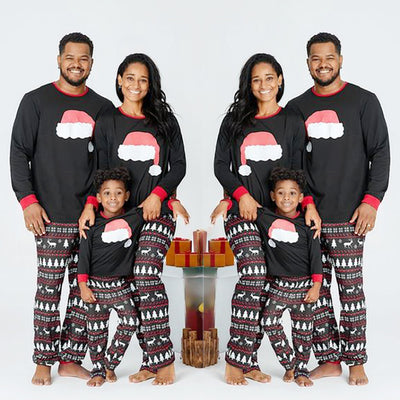 Family of three wearing matching black Christmas pajamas with Santa hat tops and reindeer fair isle pants.
