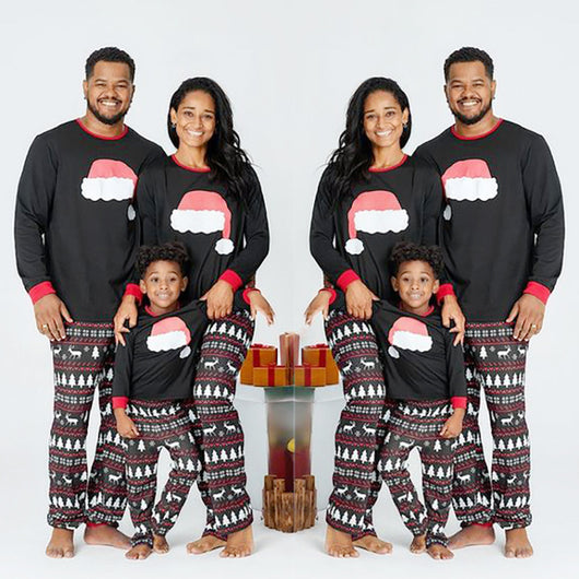 Family of three wearing matching black Christmas pajamas with Santa hat tops and reindeer fair isle pants.