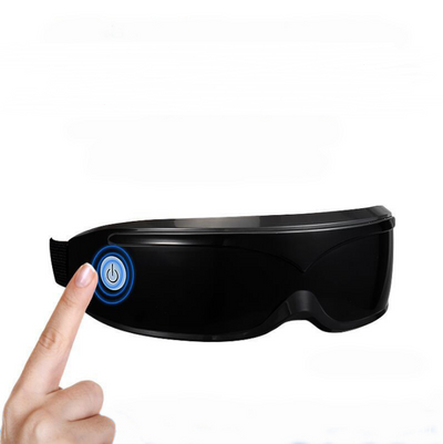 White and black eye massager with a goggle-like design, featuring a white frame and dark lenses, on a wooden surface.