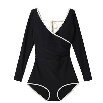 Woman wearing a black long-sleeve one-piece swimsuit with a wrap-style V-neck and light cream trim. - Image 5