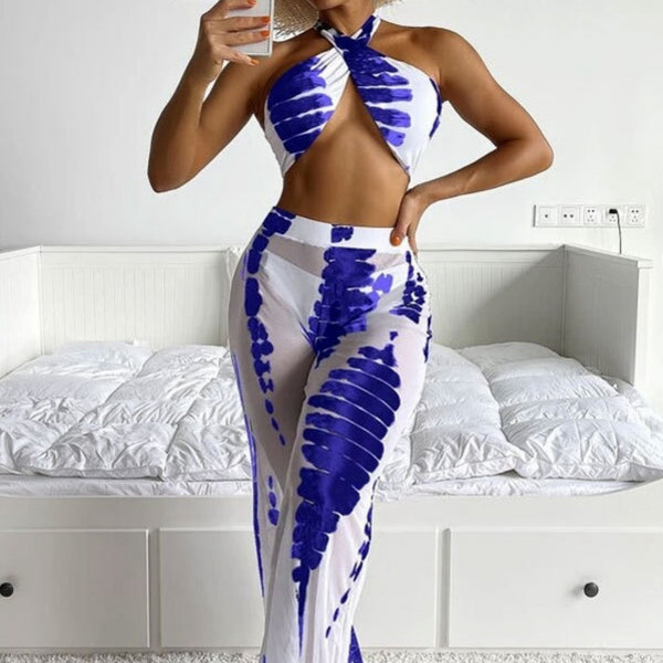 Woman in a white and blue tie-dye three-piece swimsuit set, featuring a halter bikini top, bottoms, and mesh cover-up pants.
