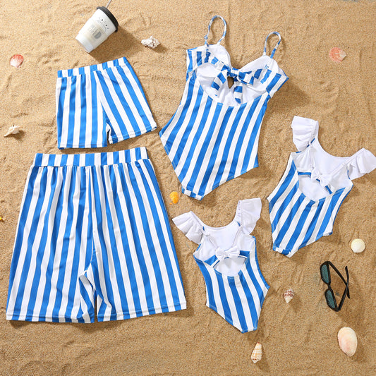 Blue and white striped one-piece swimsuit with a bow detail on the bust, laid on sand with sunglasses. - Image 2