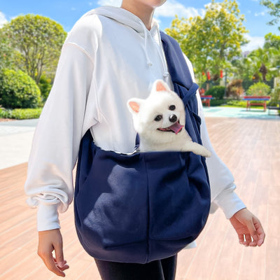 Person in white hoodie carrying a happy white dog in a navy blue pet sling bag outdoors. - Image 35