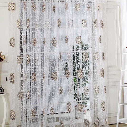 Sheer white European-style floral curtain with brown and gold patterns, hung on a gold rod in a bedroom.