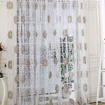 Sheer white European-style floral curtain with brown and gold patterns, hung on a gold rod in a bedroom.
