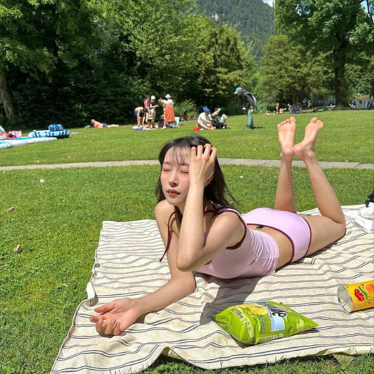 Women's light purple one-shoulder swimsuit with dark red contrast trim, lying on a striped blanket on green grass. - Image 5