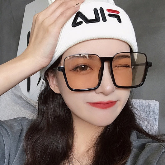 Retro square sunglasses with black frames and brown lenses held by a hand with patterned nails and a gold ring. - Image 4