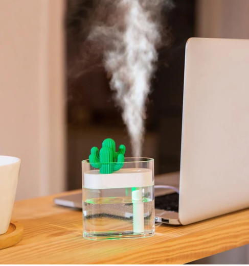 Transparent portable humidifier with a green cactus design on top, emitting mist on a wooden desk next to a laptop. - Image 3
